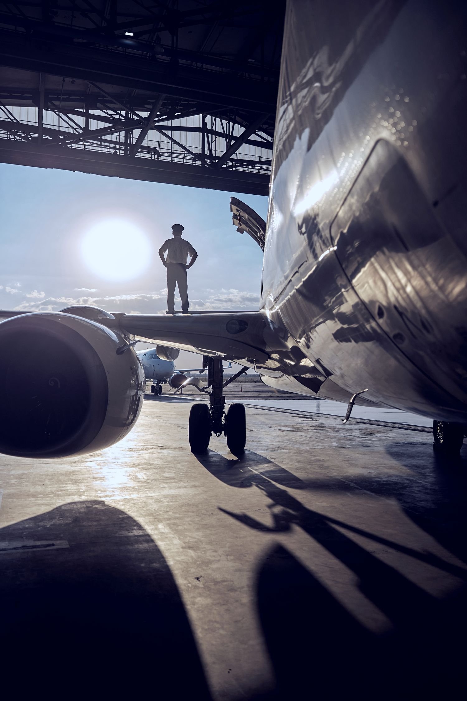 A lone figure standing beside a jet in a hangar, backlit